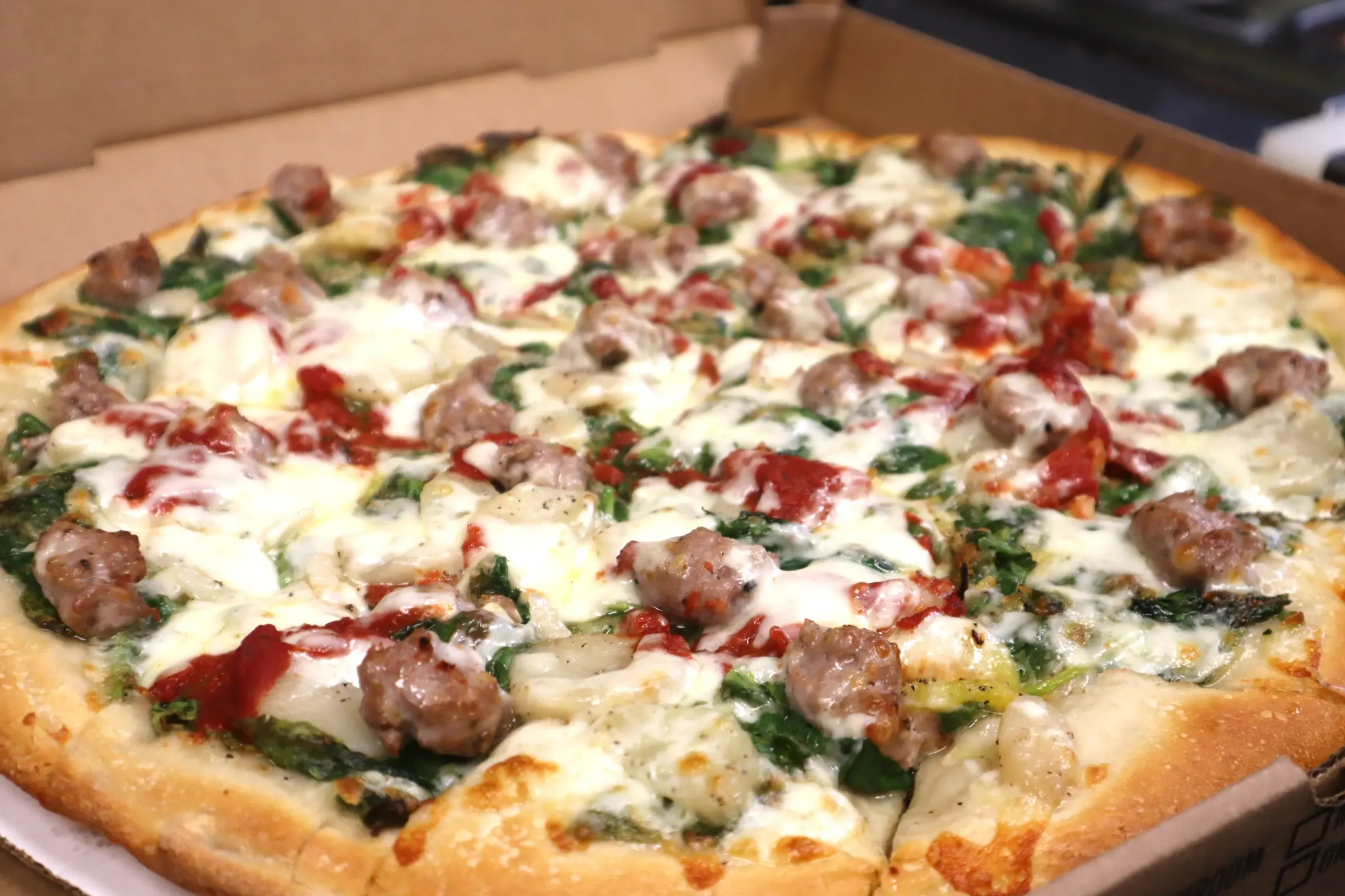 Spinach and sausage pizza in an open takeout box, puffy Greek-style crust