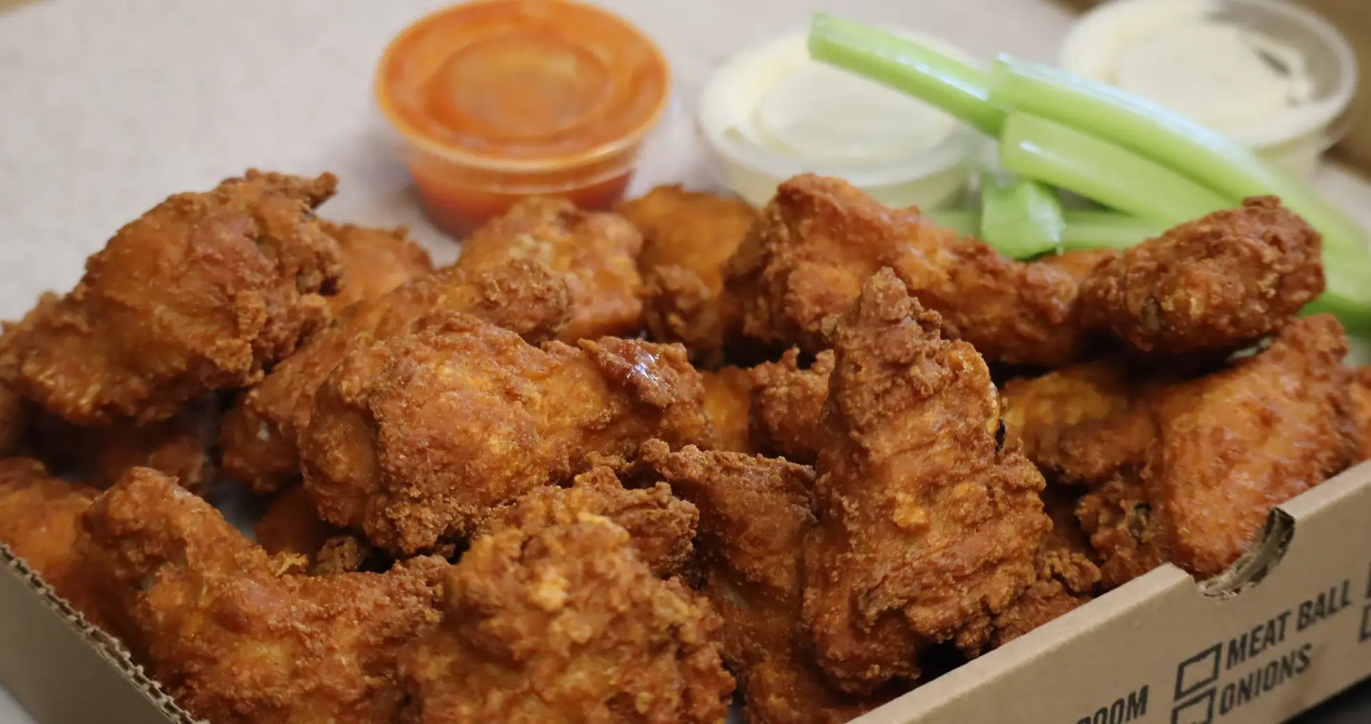 Boneless tenders in a takeout box with celery sticks and cups of blue cheese and buffalo sauce