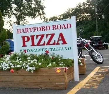 Roadside sign reading Hartford Road Pizza, Ristorante Italiano, above a planter of white flowers