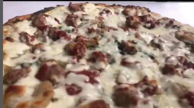 Close crop of a sausage and meat pizza covered edge to edge with melted mozzarella
