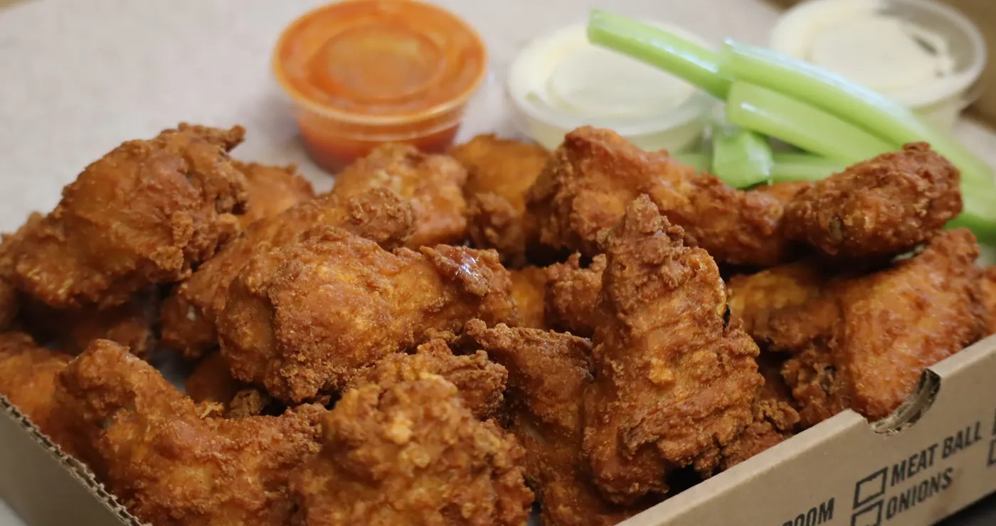 Boneless tenders in a takeout box with celery sticks and cups of blue cheese and buffalo sauce