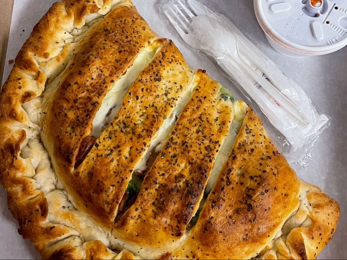 Golden baked calzone scored across the top, served with a fork and a side of sauce