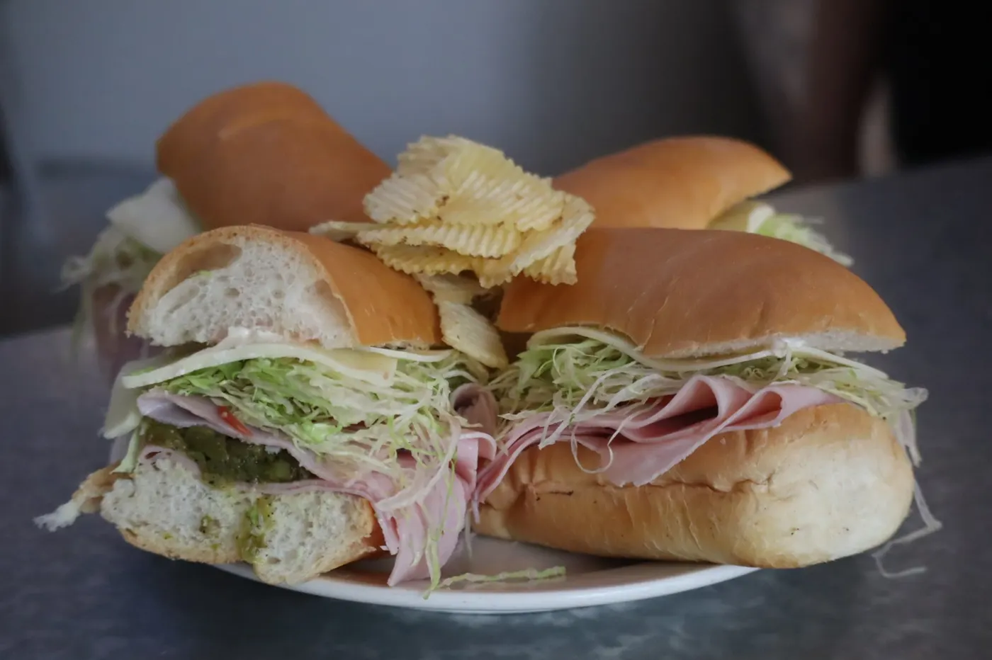 Ham and salami grinder halves on soft rolls with lettuce, served on a plate with chips