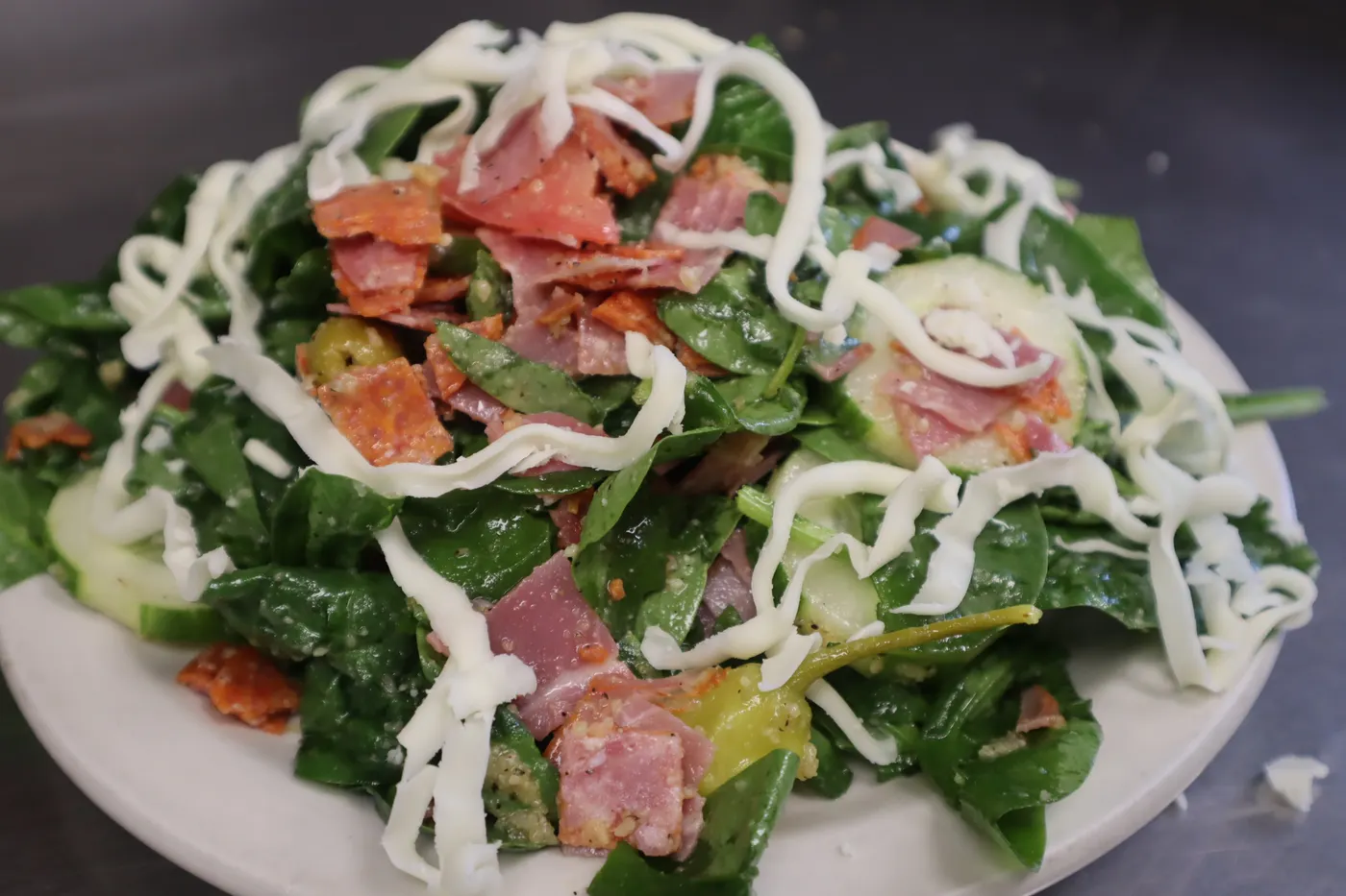 Spinach salad with bacon, tomato and shredded mozzarella under a drizzle of dressing